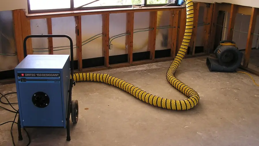 Blue dehumidifier with yellow ducting drying a room with open wall cavities